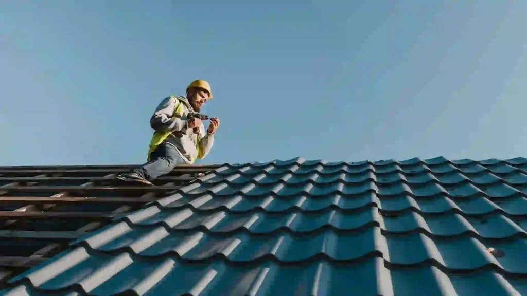 roofing contractor in Newton, Roofing contractor wearing a safety helmet and vest working on a tiled roof with a power tool.