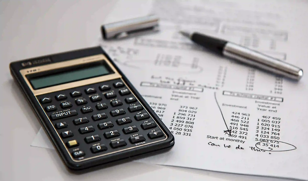 Storm Damage Roof Insurance Claims Guide for Newton, Financial calculator resting on a printed investment spreadsheet with handwritten notes and a pen.