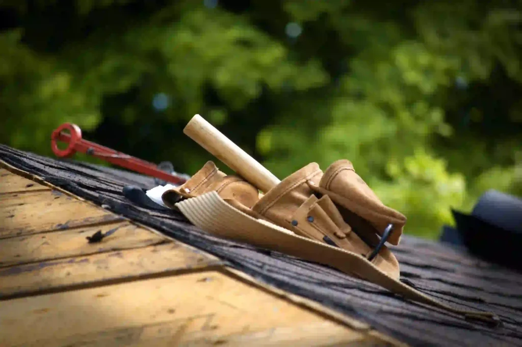 Leather roofing tool belt with a chalk line and nails resting on an asphalt shingle roof deck.