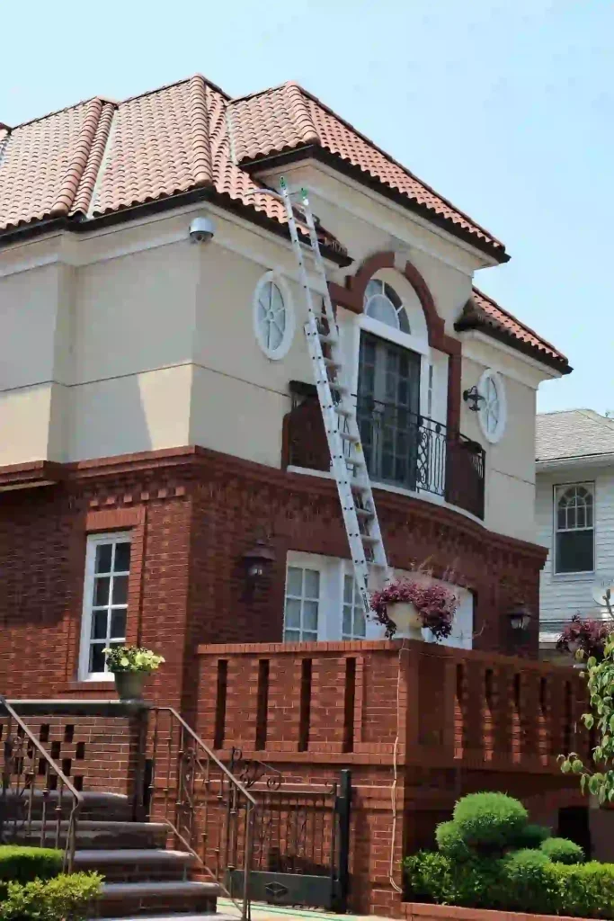 Pre-Listing Roof Inspection Newton MA,Extension ladder leaning against a brick house with a curved clay tile roof and arched second-floor balcony.