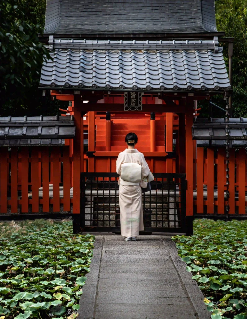 Metal Roof vs Shingle Massachusetts, Woman in a white kimono standing before the gate of a Japanese shrine with a tiled roof and vermillion wooden structure.