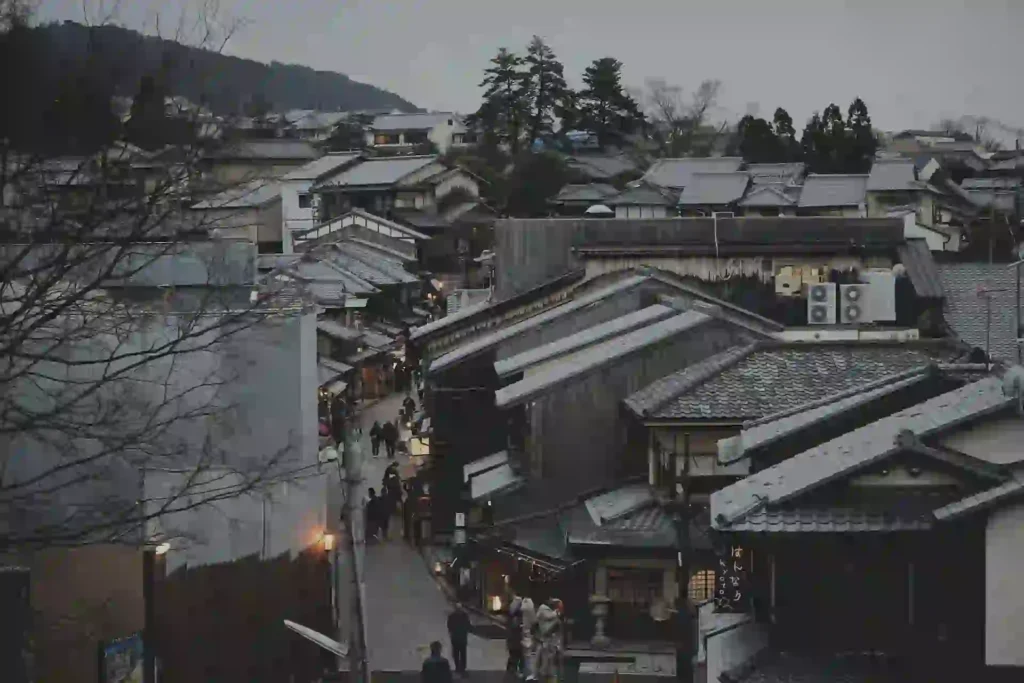 Overhead view of a traditional Japanese street lined with tiled rooftops at dusk, with pedestrians walking below.