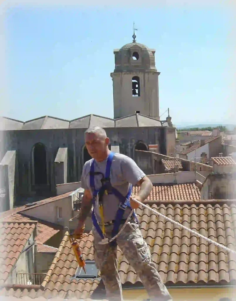 Roofer in a safety harness working on clay tile roofs with a European bell tower visible in the background.