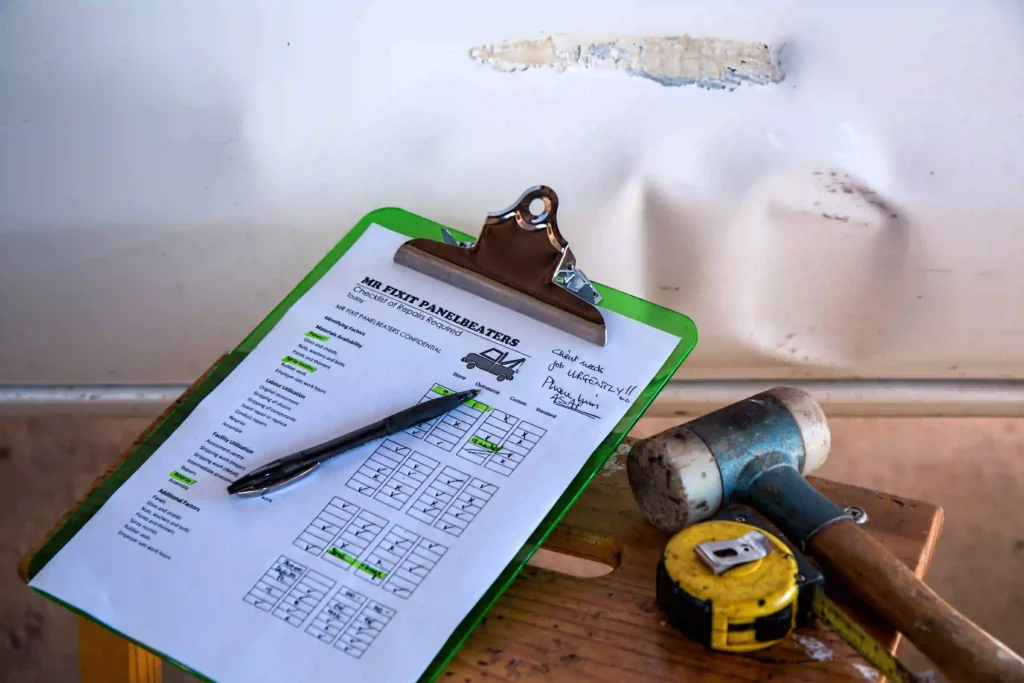 Repair estimate checklist on a clipboard with a pen, tape measure, and mallet, set against a wall with peeling paint.
